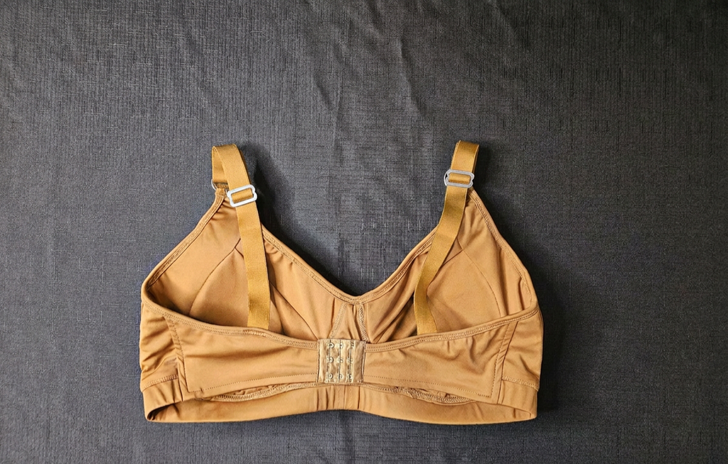 A tan molded-cup bra laid flat on a dark gray textured fabric background.