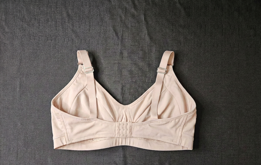 A beige wireless bra with adjustable shoulder straps and a center gore, laid flat on a dark gray textured fabric background.