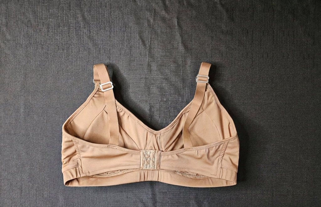 A beige wireless bra laid flat on a dark gray textured fabric background.