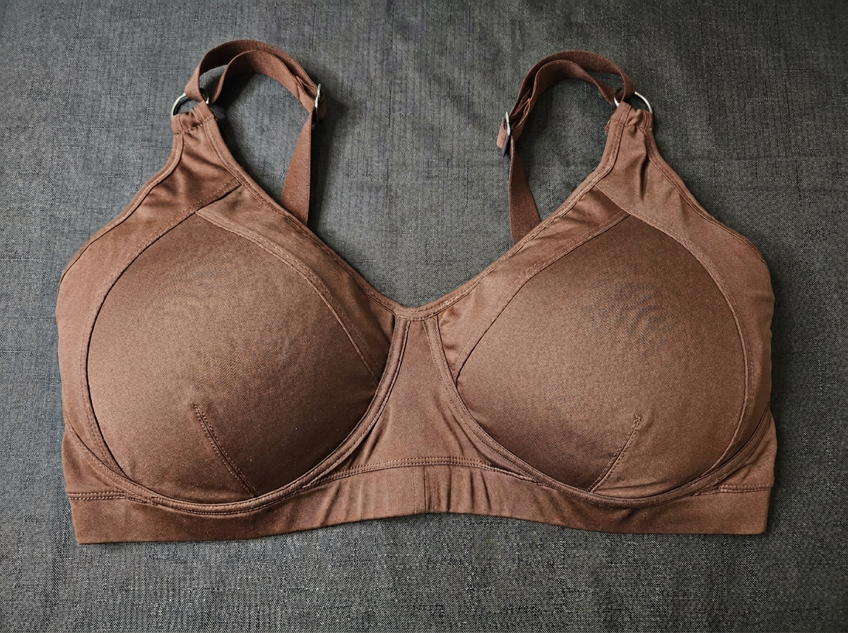 A brown wireless bra with wide shoulder straps and a wide underband, laid flat on a textured gray fabric background.
