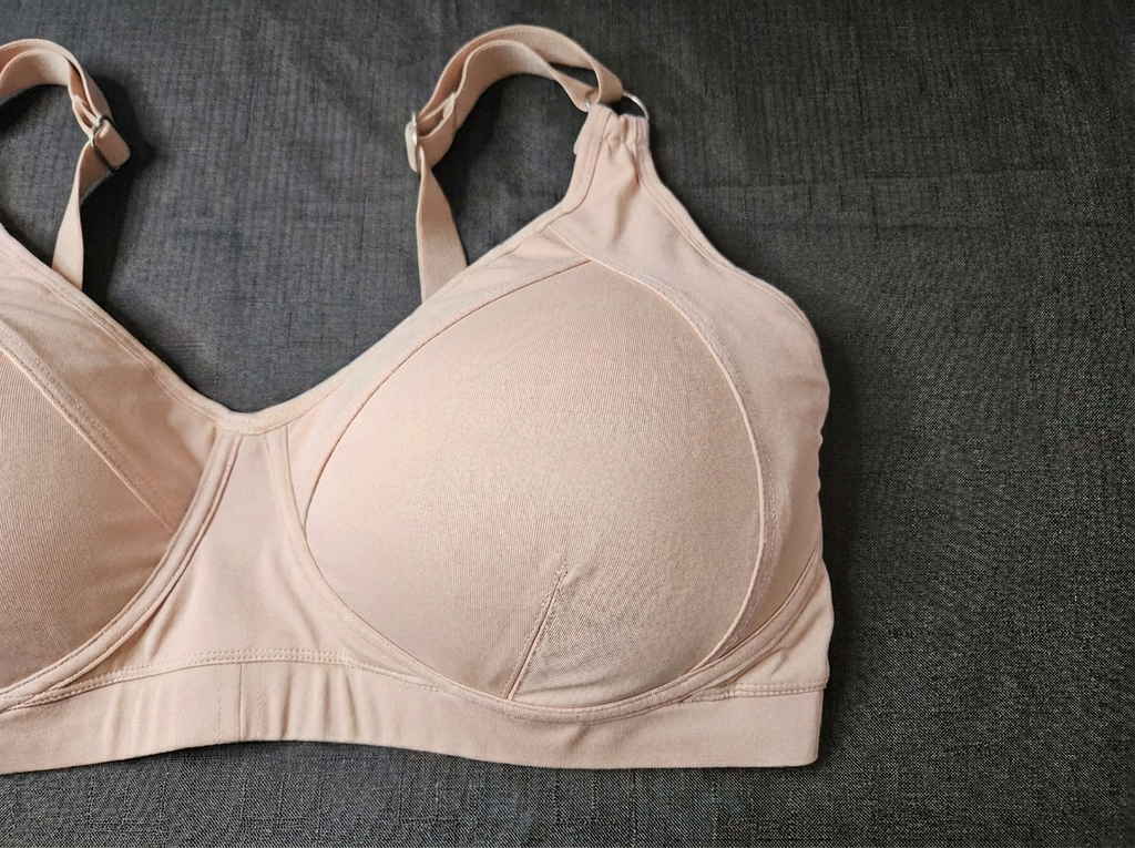 A light beige wireless bra with wide shoulder straps, laid flat on a dark gray textured fabric background.
