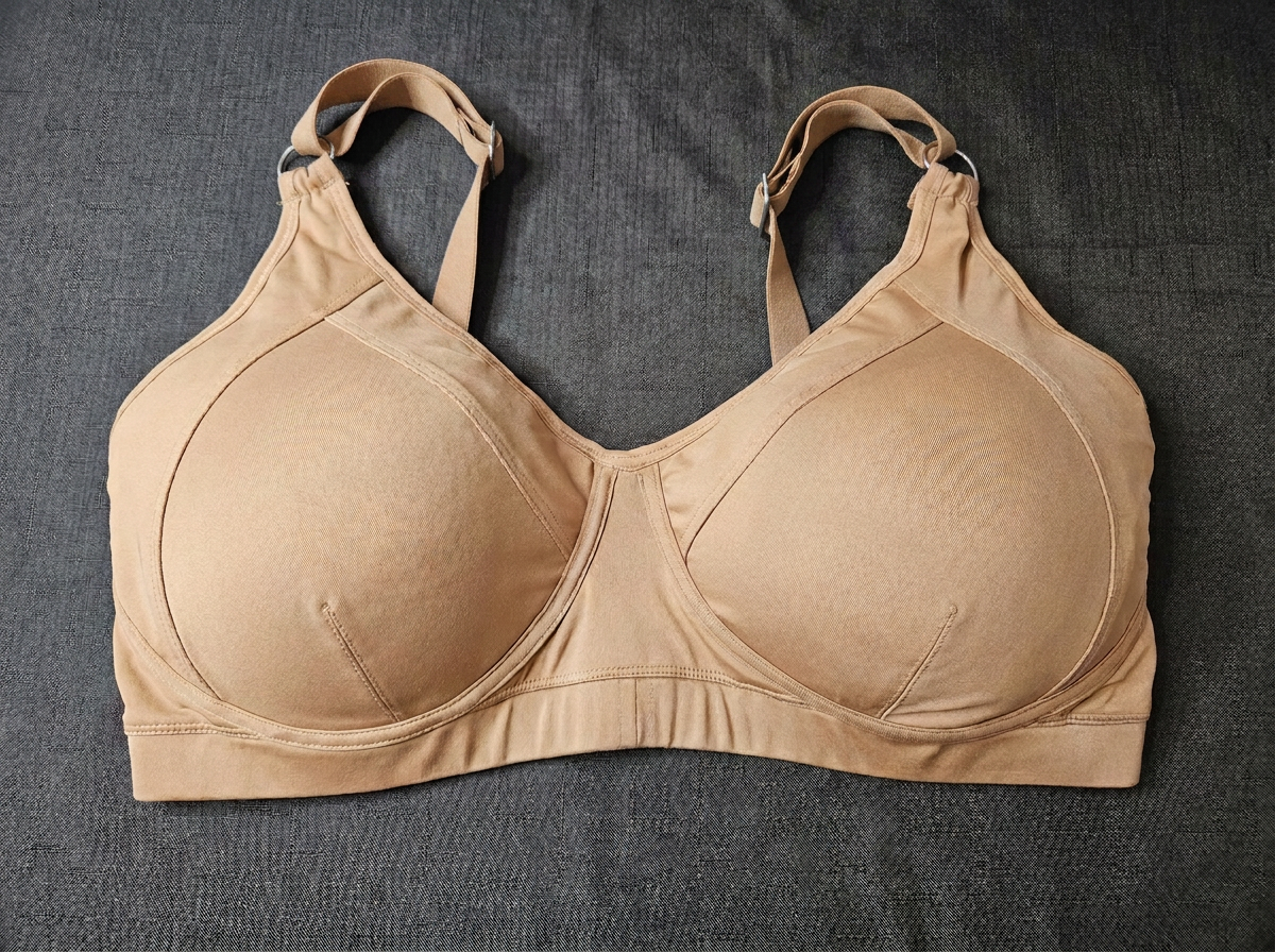 A beige wireless bra with wide shoulder straps and a wide underband, laid flat on a dark gray textured fabric background.