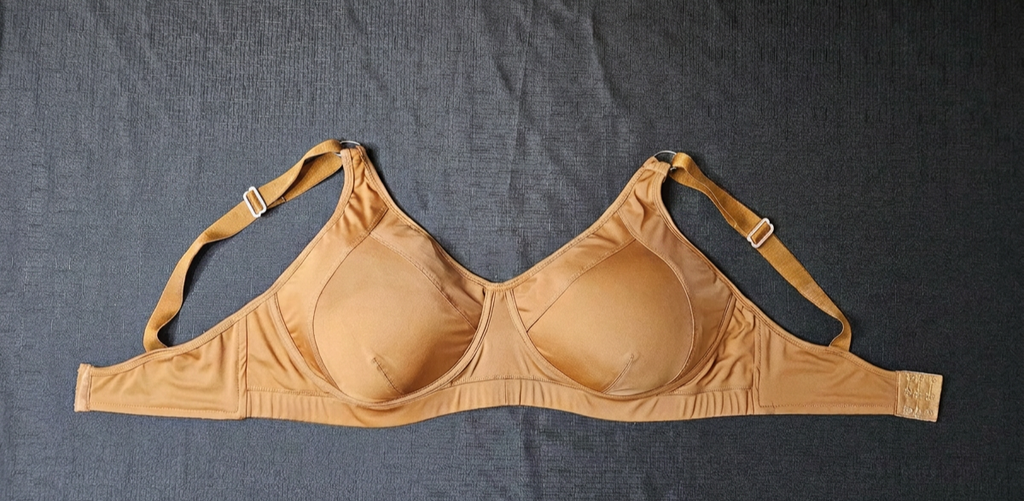 A tan wireless underwire bra laid flat on a dark gray textured fabric background.