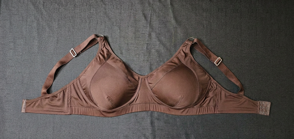 A brown seamless underwire bra laid flat on a textured gray fabric background.