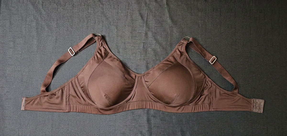 A brown seamless underwire bra laid flat on a textured gray fabric background.