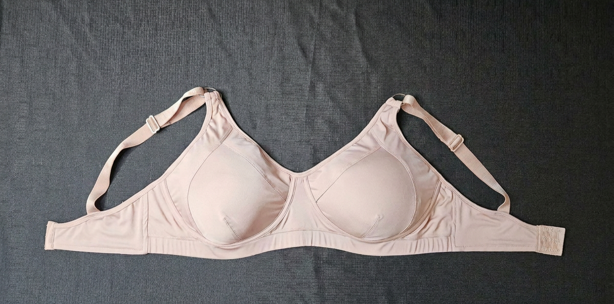 A light beige wireless bra laid flat on a dark gray textured fabric background.