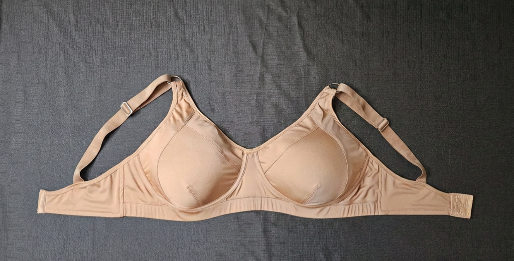 A beige wireless bra laid flat on a dark gray textured fabric background.