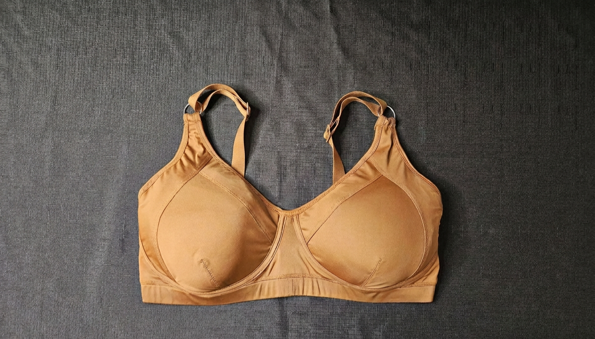 A tan molded-cup bra laid flat on a dark gray textured fabric background.