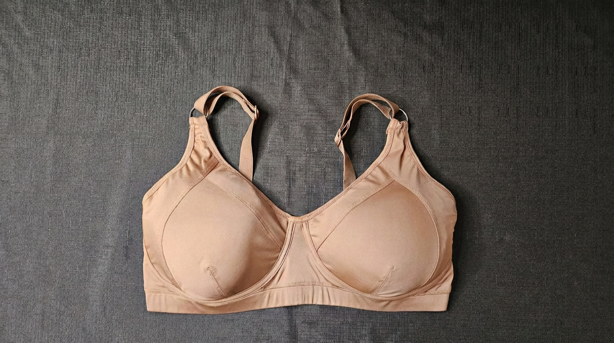 A beige wireless bra with adjustable shoulder straps, laid flat on a dark gray textured fabric background.